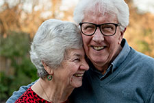 An elderly couple stands close together and smiles